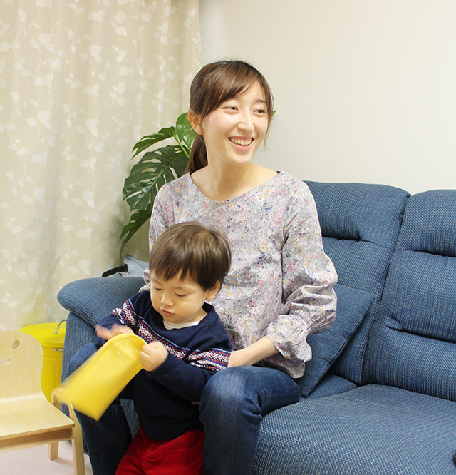 何かで遊んでいる子供とソファに座ってインタビューに答える中村様